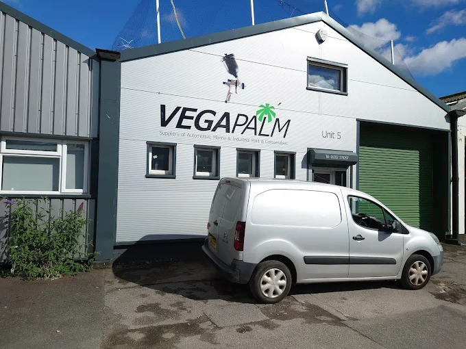 A white building with a green shutter and a white van parked in front. The building has a large sign with black letters th...